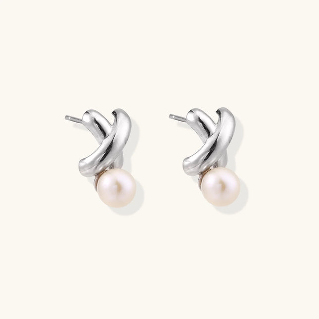 Rhodium-plated silver earrings with twisted X design and freshwater pearl drops on beige background