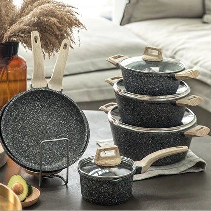 Set of black speckled cookware with wooden handles on a kitchen counter.